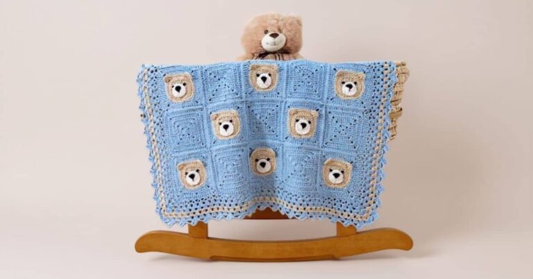 Manta de crochê azul para bebê com desenho de ursinhos e um ursinho de pelúcia em cima.