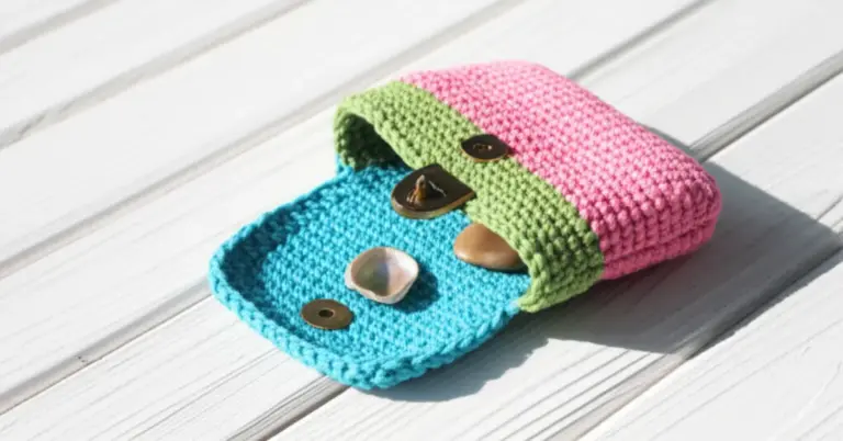 Bolsinha de crochê infantil aberta, com interior azul e detalhes coloridos, sobre uma superfície de madeira clara.