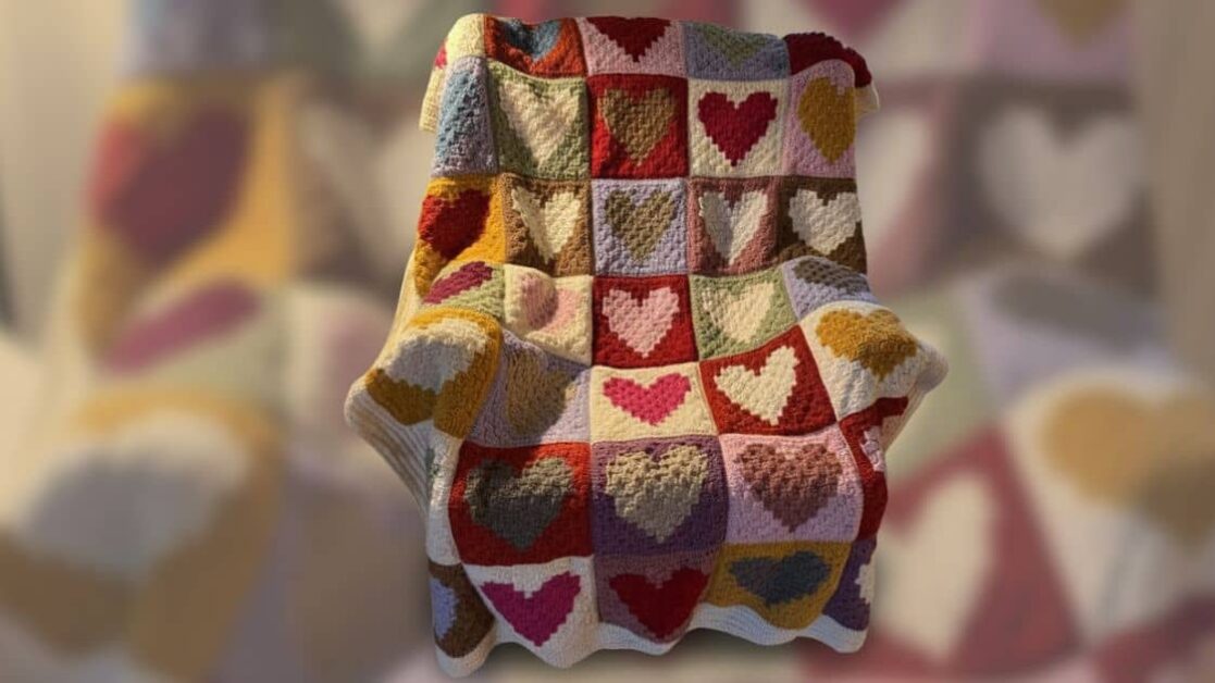 Manta de crochê granny square com padrão de corações coloridos sobre uma cadeira.