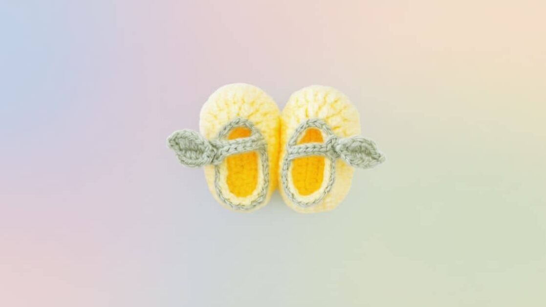 Um par de sapatinhos de bebê em crochê, com cores que lembram um limão siciliano, repousam lado a lado.