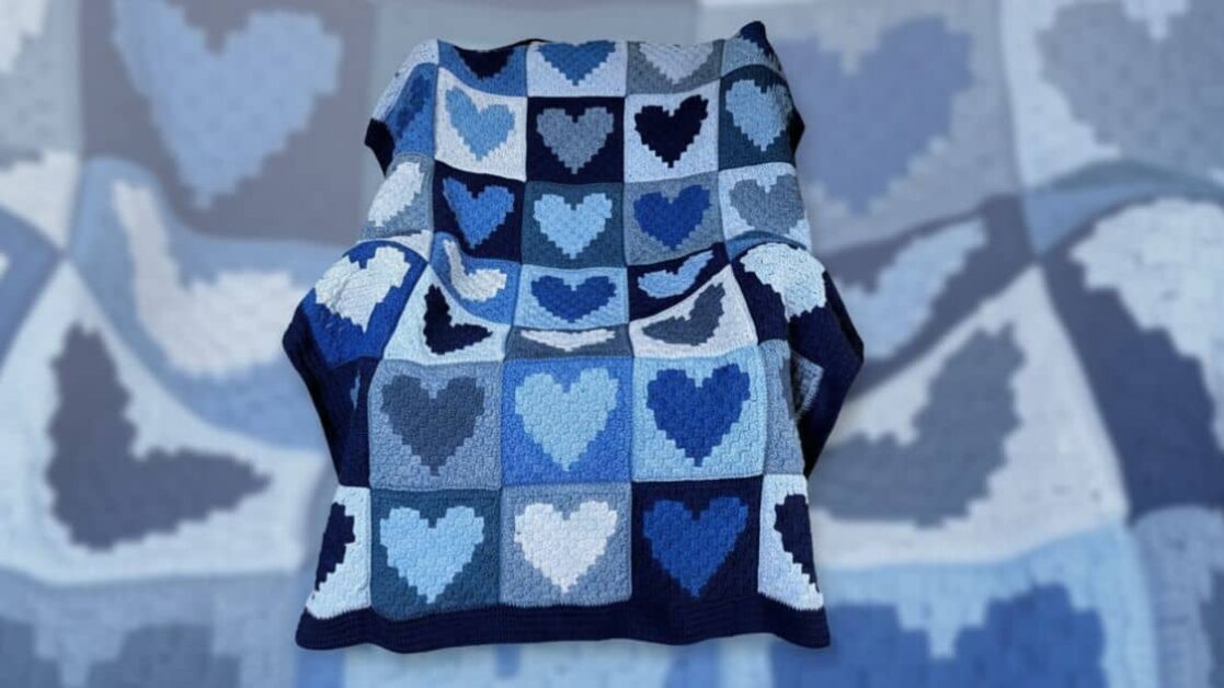 Manta de crochê azul com padrão de corações granny square sobre uma cadeira.