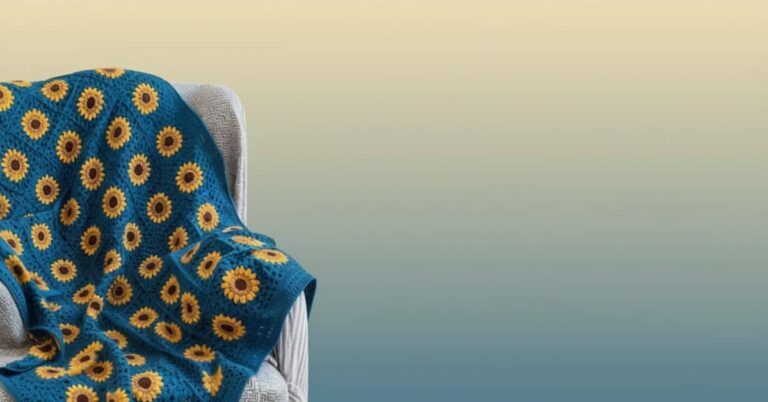 Manta de crochê azul com margaridas amarelas e centros marrons sobre uma poltrona.