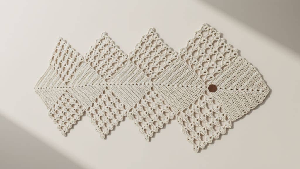 Caminho de mesa de crochê bege com design em zigue-zague e acabamento pontudo, sobre fundo liso bege.