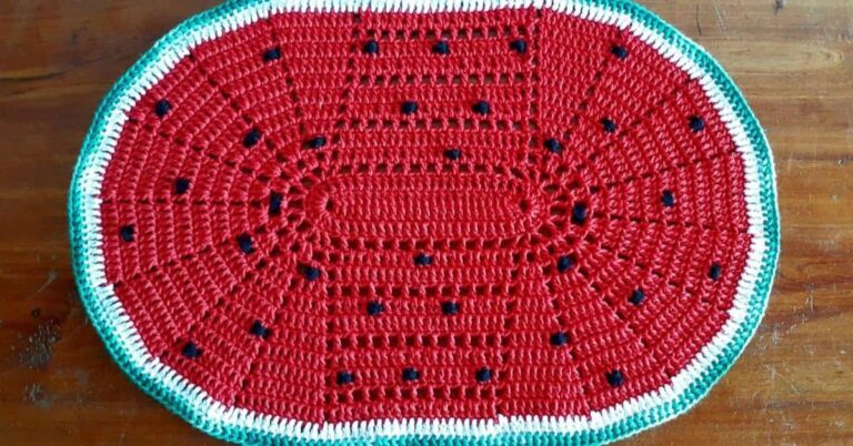 Tapete oval de crochê com design de fatia de melancia: centro vermelho com sementes pretas e borda verde e branca.